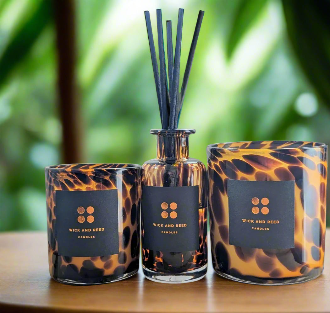 Two tortoiseshell-patterned candles and a diffuser with 'Wick and Reed' branding on a wooden surface.